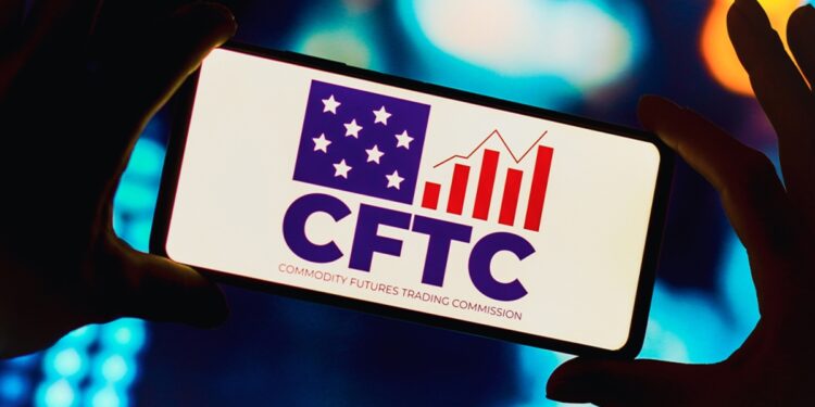 Par de manos sujetando un teléfono que refleja el logo de la CFTC.