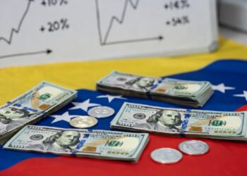 Dólares en una mesa con la bandera de Venezuela, con algunas monedas de USDT, y un pizarrón de gráficas alcistas.