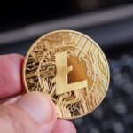Una mano sostiene una moneda dorada de litecoin.