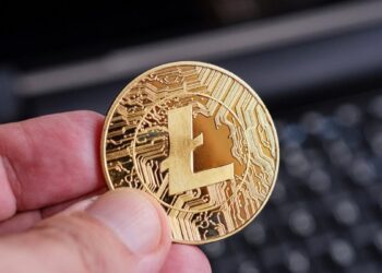 Una mano sostiene una moneda dorada de litecoin.