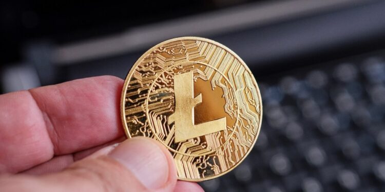 Una mano sostiene una moneda dorada de litecoin.