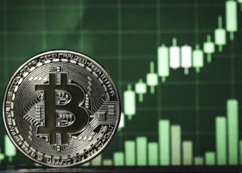 Moneda física de bitcoin en primer plano y gráfico de velas verdes alcista de fondo, representando subida de precio.