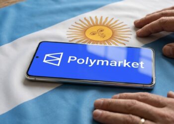 Teléfono inteligente que muestra el logo de Polymarket sobre una bandera de Argentina y con dos manos al lado.