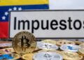 Monedas físicas de bitcoin y criptomonedas, junto a la bandera de Venezuela y un cartel que dice "Impuestos".