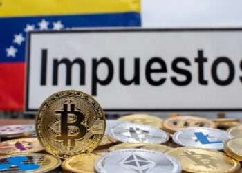 Monedas físicas de bitcoin y criptomonedas, junto a la bandera de Venezuela y un cartel que dice "Impuestos".