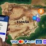 Teléfono celular y criptomonedas sobre el mapa de España al fondo.