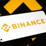 Logo de Binance atrás con el logo de Binance en un teléfono inteligente