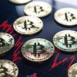 Monedas físicas de bitcoin reposando sobre un gráfico de velas rojo intenso que muestra una fuerte tendencia bajista.