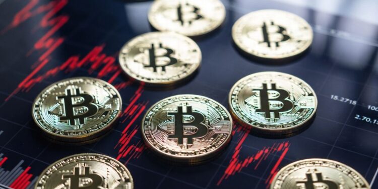 Monedas físicas de bitcoin reposando sobre un gráfico de velas rojo intenso que muestra una fuerte tendencia bajista.