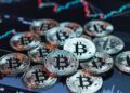 Monedas físicas de bitcoin sobre una pantalla con gráficos de precios.