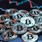 Monedas físicas de bitcoin sobre una pantalla con gráficos de precios.