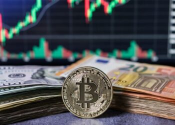 Moneda física de bitcoin rodeada de billetes de dólares y euros sobre un fondo con gráficos bursátiles.