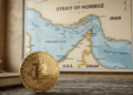 En primer plano, sobre una mesa, hay una moneda física de bitcoin. En el fondo, se ve un mapa del estrecho de Ormuz.