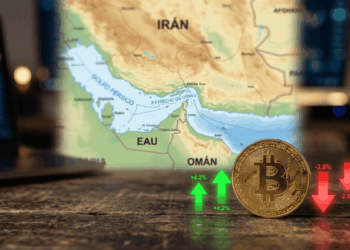 En primer plano, moneda física de bitcoin con flechas hacia arriba y hacia abajo. En el fondo: mapa del estrecho de Ormuz.