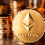 Monedas físicas de ether en un escritorio con más monedas apiladas en el fondo.