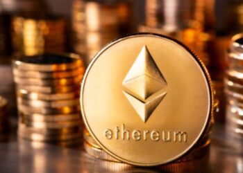 Monedas físicas de ether en un escritorio con más monedas apiladas en el fondo.