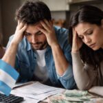 Personas tomándose la cabeza delante de un escritorio donde se ve la bandera de Argentina.