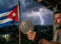 Un hombre sosteniendo una moneda física de bitcoin en la mano, junto a la bandera de Cuba a un lado y un rayo cayendo en el fondo.