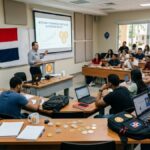 Salón de clases con universitarios, bitcoin alrededor y la bandera de República Dominicana.
