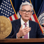 Jerome Powell hablando en un discurso, con una moneda física de bitcoin sobre su atril.