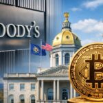 El cartel de Moody's junto a un edificio y a una moneda física de bitcoin.