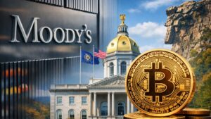 El cartel de Moody's junto a un edificio y a una moneda física de bitcoin.