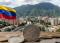 Monedas que tienen grabado la frase "stablecoin venezolana", de fondo la bandera de Venezuela y la ciudad de Caracas.