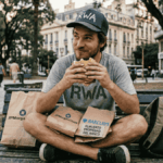 Un hombre con la inscripción "RWA" en su camisa y gorra, comiéndole un sandwich robado a los bancos.