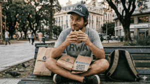 Un hombre con la inscripciรณn "RWA" en su camisa y gorra, comiรฉndole un sandwich robado a los bancos.