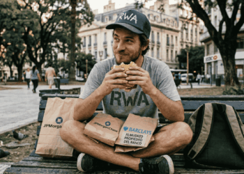 Un hombre con la inscripción "RWA" en su camisa y gorra, comiéndole un sandwich robado a los bancos.