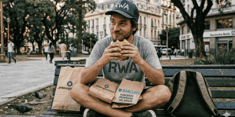 Un hombre con la inscripción "RWA" en su camisa y gorra, comiéndole un sandwich robado a los bancos.