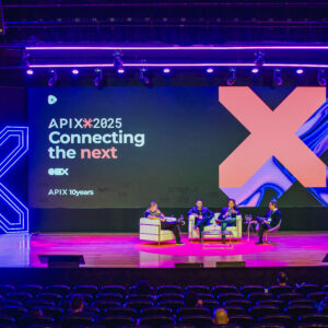 Escenario de conferencia con panelistas, pantalla gigante con texto e iluminación neón.