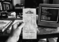 Fotografía histórica en blanco y negro que muestra una mano sosteniendo en primer plano un recibo de Papa John's fechado el 22 de mayo de 2010 con la inscripción "10,000 BTC transferred". Al fondo, sobre una mesa de madera rústica, se observan cajas de pizza y un monitor CRT antiguo de computadora de escritorio.