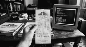 Fotografía histórica en blanco y negro que muestra una mano sosteniendo en primer plano un recibo de Papa John's fechado el 22 de mayo de 2010 con la inscripción "10,000 BTC transferred". Al fondo, sobre una mesa de madera rústica, se observan cajas de pizza y un monitor CRT antiguo de computadora de escritorio.