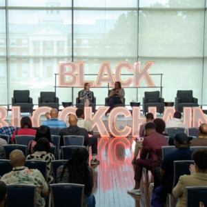 Conferencia sobre "Black Blockchain" con panelistas en el escenario y audiencia en formato horizontal.