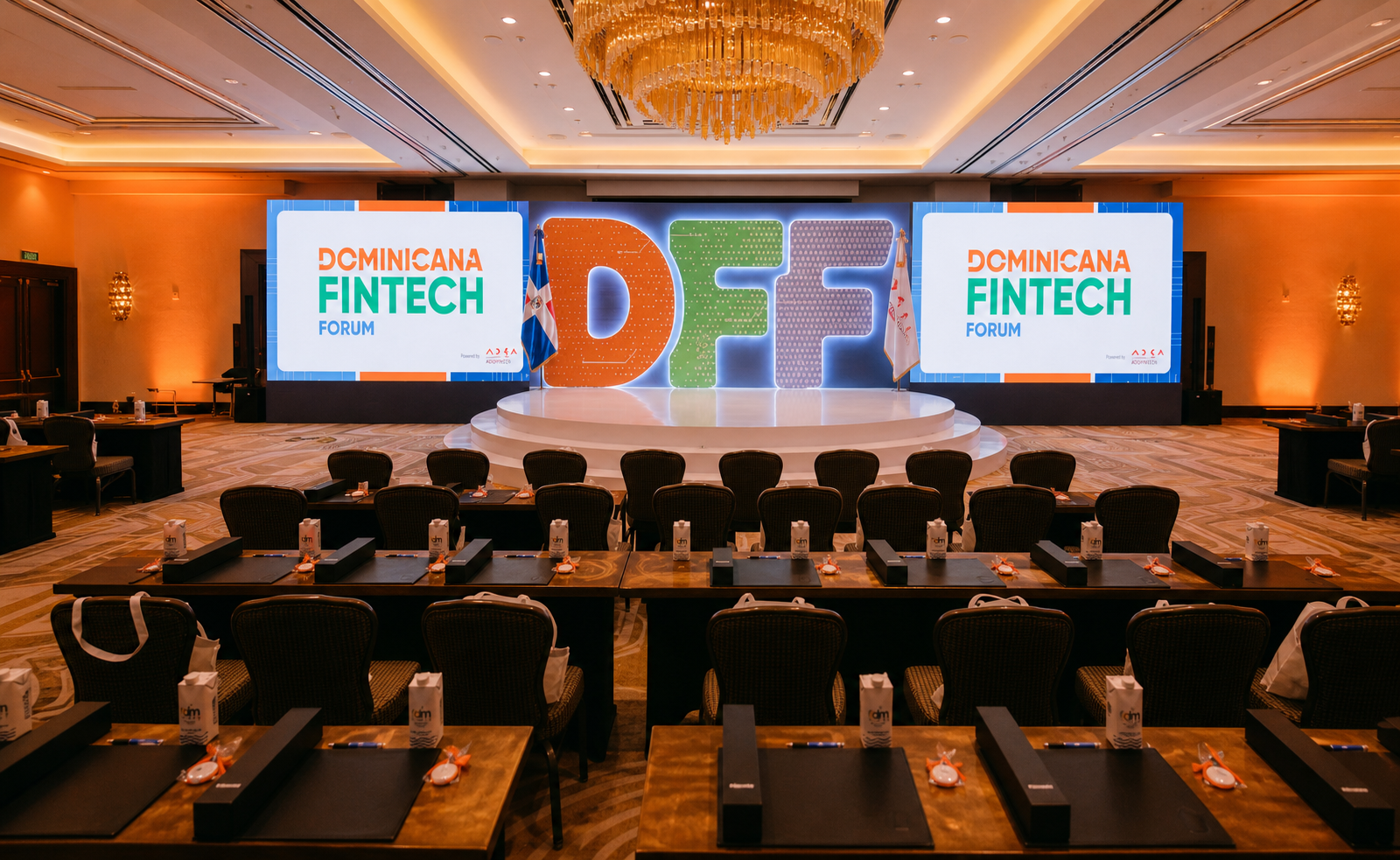 Sala de conferencia del Dominicana Fintech Forum con escenario iluminado, letras DFF y ambiente corporativo cálido.