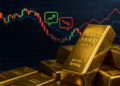 Lingotes de oro apilados frente a gráfico financiero con velas rojas y verdes, reflejando volatilidad y reciente caída del precio.