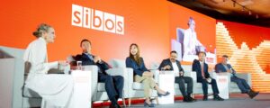 Panelistas en un escenario debatiendo en el evento financiero "Sibos" con fondo color naranja.