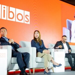 Panelistas en un escenario debatiendo en el evento financiero "Sibos" con fondo color naranja.