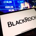 Un celular que muestra el logo de BlackRock delante de una pantalla de precios.