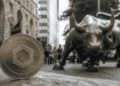 En primer plano: moneda fรญsica con el logo de Chainlink. En el fondo: imรกgenes tรญpicas de Wall Street.