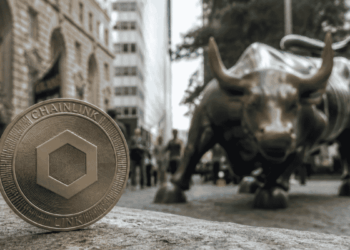 En primer plano: moneda física con el logo de Chainlink. En el fondo: imágenes típicas de Wall Street.