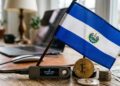 Una hardware wallet con bitcoin y la bandera de El Salvador sobre un escritorio.