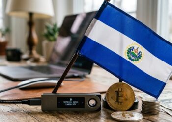 Una hardware wallet con bitcoin y la bandera de El Salvador sobre un escritorio.