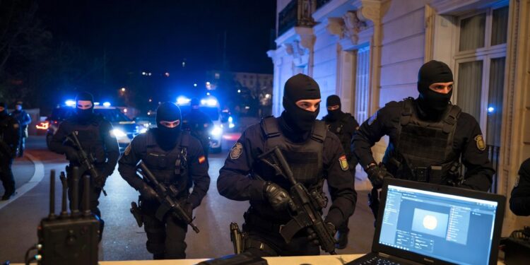 Operación policial en España varios agentes de la Policía Nacional con chalecos antibalas y pasamontañas irrumpiendo en una vivienda de lujo durante la noche. Luces azules de patrullas policiales iluminando la escena.