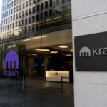Entrada de oficinas corporativas de Kraken con fachada de vidrio, logotipo de la empresa y una bandera de Estados Unidos en el exterior