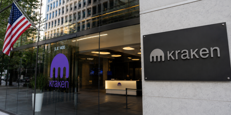 Entrada de oficinas corporativas de Kraken con fachada de vidrio, logotipo de la empresa y una bandera de Estados Unidos en el exterior