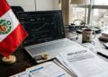 Escritorio con una laptop, una moneda física de bitcoin dorada, la bandera de Perú y documentos de impuestos.