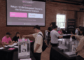 Representación de una votación en un centro físico, con personas depositando sus votos en urnas, generada por inteligencia artificial.