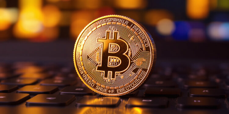 Moneda de Bitcoin en primer plano, sobre una laptop con desenfoque de campo que hace que la pantalla se vea como luces y destellos